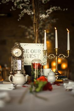 a table with candles, teapots and a sign that says be our guest