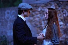 a man and woman standing next to each other in front of a stone wall at night