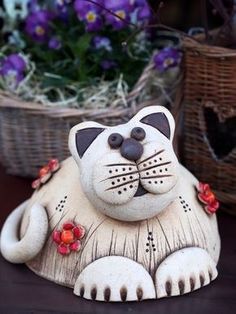 a ceramic cat sitting on top of a wooden table next to baskets with purple flowers