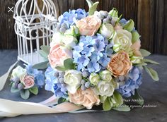 a bridal bouquet with blue, peach and white flowers sits next to a birdcage