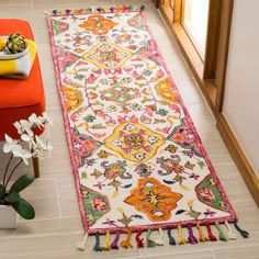 a colorful runner rug in the middle of a room with an orange chair and potted plant