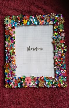 a photo frame covered in lots of different colored beads and buttons on a red surface