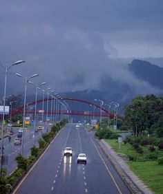 cars driving down the road in front of a bridge with mountains in the back ground