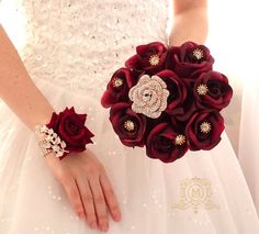 a woman in a wedding dress holding a bouquet of red roses and brooches