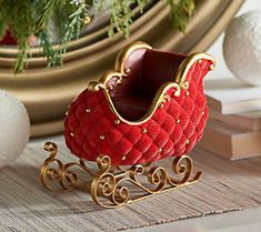 a red and gold miniature sleigh sitting on top of a wooden table next to ornaments