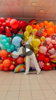 a man standing in front of a large amount of balloons on the floor with his hands up