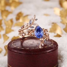 a gold ring with a blue stone surrounded by white and clear stones on top of a wooden box