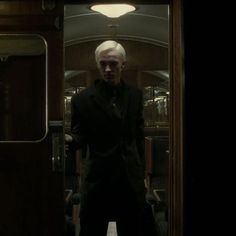 a man with white hair standing in front of a door on a subway car at night