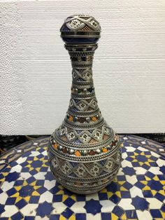 a decorative vase sitting on top of a colorful tablecloth covered floor with white and blue tiles