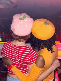 two women hugging each other in front of a neon bar with fruit on the back