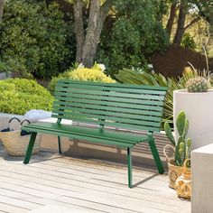 a green bench sitting on top of a wooden deck next to plants and potted plants