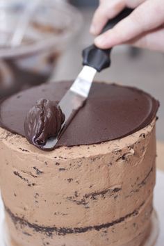 a person is spreading chocolate frosting on a cake