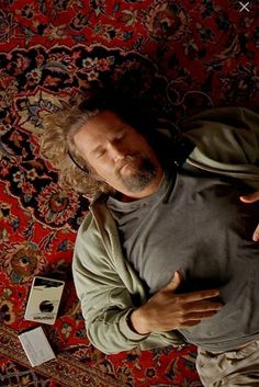 a man laying on top of a rug next to a cell phone and remote control