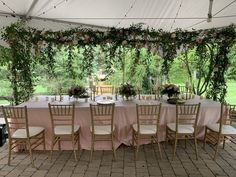 a table set up under a tent with flowers and greenery