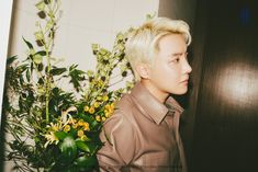 a man with blonde hair standing in front of a flower pot and looking off into the distance