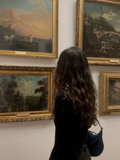 a woman standing in front of paintings on the wall and looking at them with her back to the camera