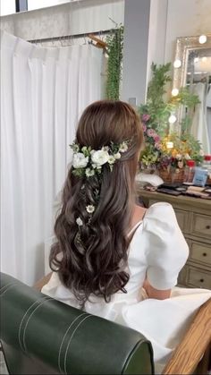 a woman sitting in front of a mirror with flowers in her hair