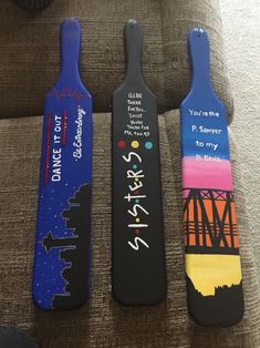 three wooden paddles with different designs painted on them sitting on a couch in a living room