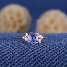 a tan gold ring with an oval blue sapphire surrounded by pearls and other stones on a blue cloth