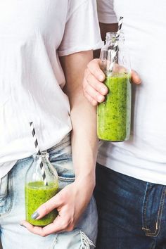 two people holding mason jars filled with green smoothies