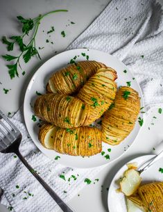 some potato wedges are on a white plate next to a fork and spoon with parsley