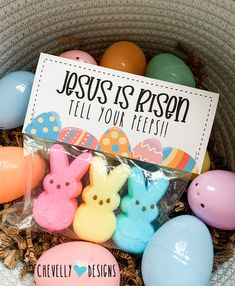 a basket filled with easter eggs and peeps on top of each other, next to a sign that says jesus is risen tell your flesh