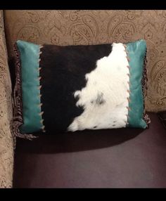 a cowhide pillow sitting on top of a brown chair next to a black and white pillow