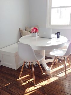 a white table and chairs in a small room with wood flooring next to a window