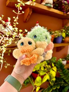 a hand holding a small stuffed animal in front of some potted plants