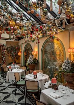 an indoor dining area decorated for christmas with ornaments hanging from the ceiling and tables covered in white tablecloths