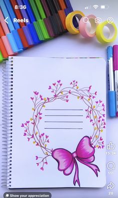 an open notebook with a pink bow on it next to markers, pens and markers