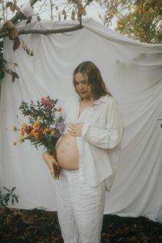 a pregnant woman holding flowers in front of a white backdrop