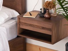 a nightstand with a notepad, pen and plant on it next to a bed