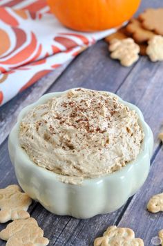 a bowl filled with cream cheese surrounded by crackers and an orange in the background