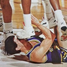 a basketball player laying on the floor with his feet up in the air and other players standing behind him