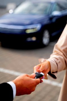 two people exchanging keys to each other in front of a blue car on the street