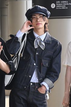 a young man wearing glasses and a denim jacket talking on a cell phone while walking down the street