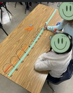 two children sitting at a table with faces drawn on the board and pencils in front of them