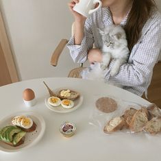 a woman sitting at a table holding a cup and drinking coffee with her cat on her lap