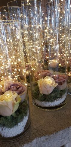 three glass vases filled with flowers and moss on top of a table covered in lights