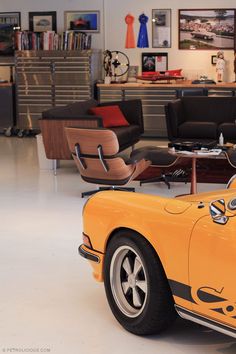 an orange sports car is parked in a room with black chairs and pictures on the wall