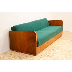 a green couch sitting on top of a hard wood floor next to a white wall