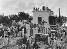 an old black and white photo of people standing on top of a building with a car parked in front of it