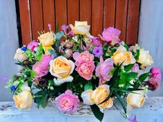 a basket filled with lots of pink and yellow flowers on top of a table next to a wooden door