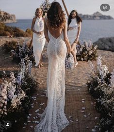 two women in white dresses walking down a path next to some flowers and lavenders