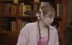 a woman with braids and a pink shirt is standing in front of bookshelves