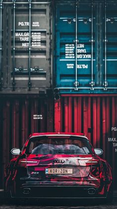 a red car parked in front of some shipping containers