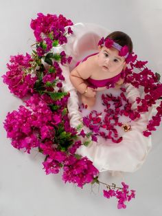 a baby in a dress surrounded by pink flowers