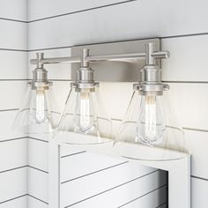 two light bathroom fixture with clear glass shades on the mirror and white paneled wall