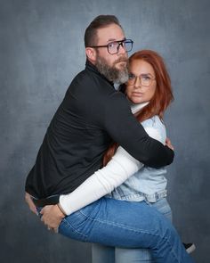 a man and woman hugging each other in front of a gray background with one holding the other